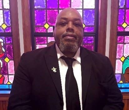 Bearded man in black suit by stained glass