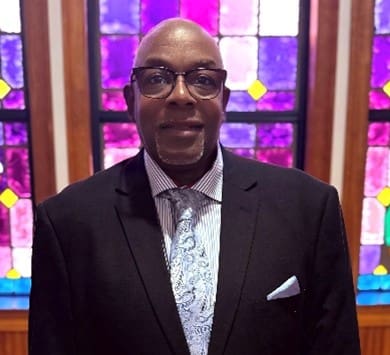 Person in suit and tie before stained-glass window