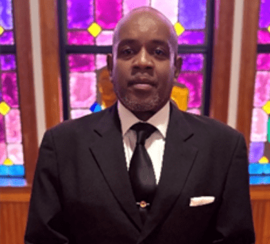Man in black suit before purple stained glass